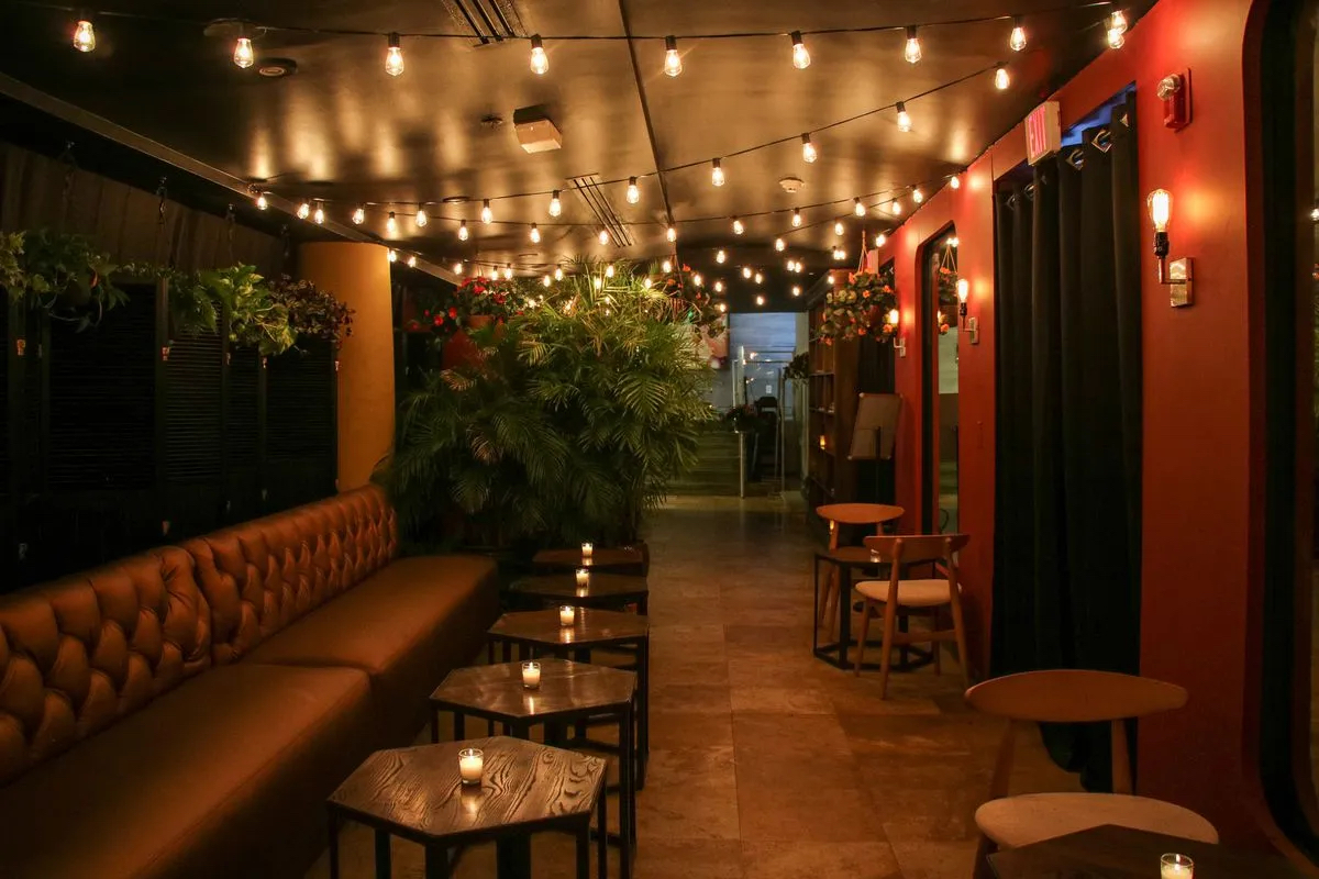 Bench seating and candle lit bistro tables lining hallway with edison bulb string lights lining the ceiling