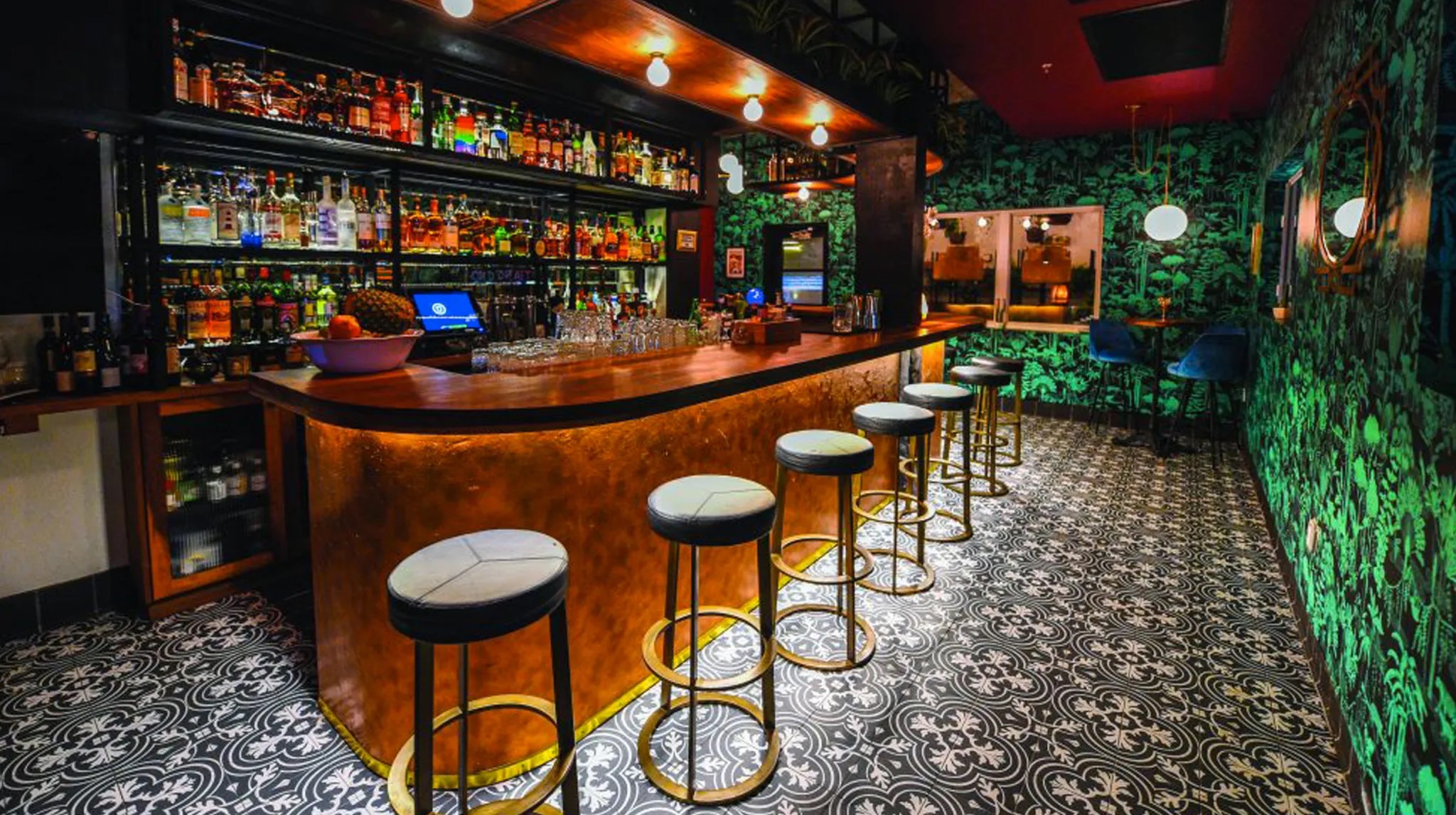 Leather topped brass bar stools lining a wooden topped bar with liquor shelves behind